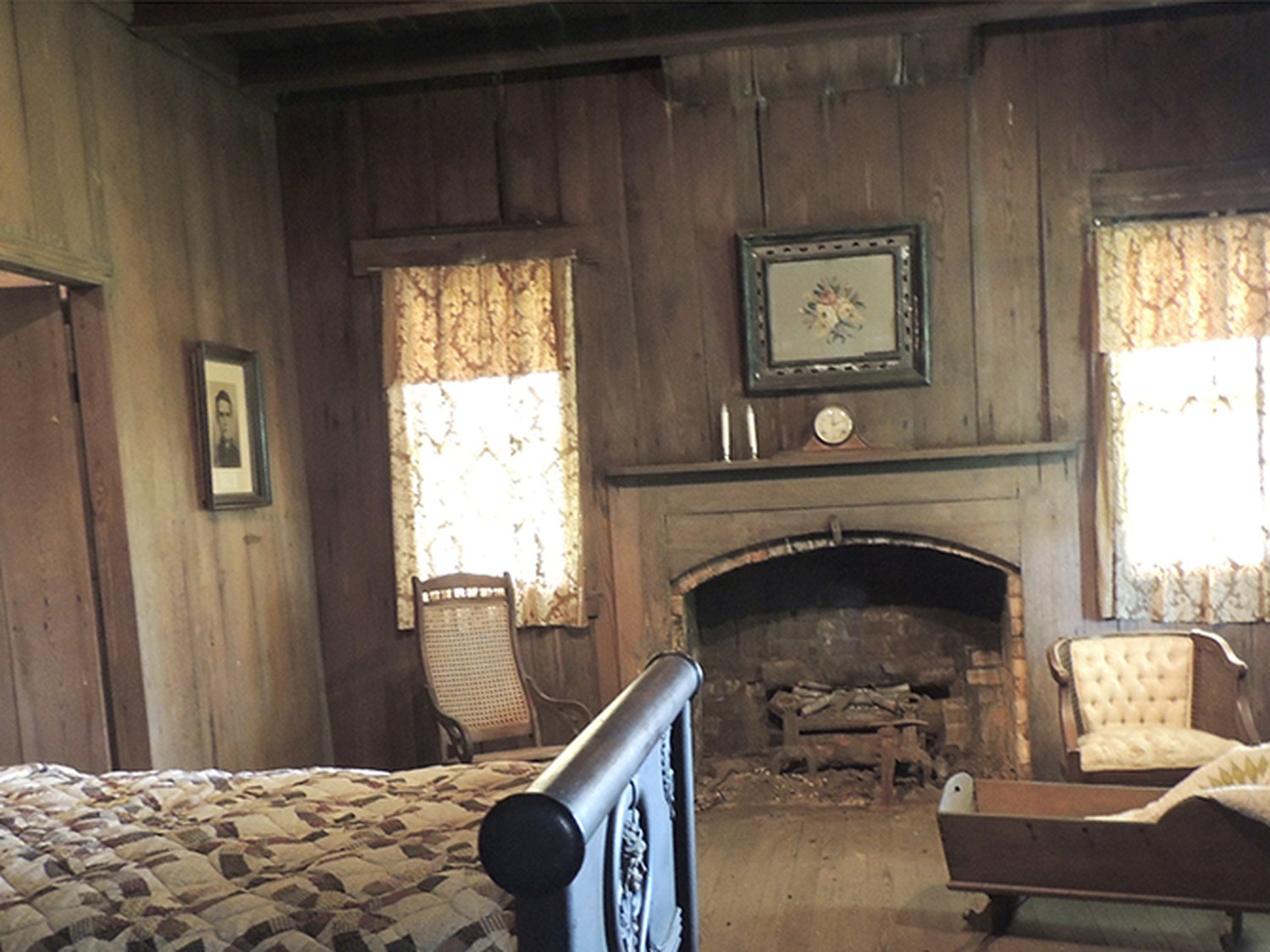 A period bedroom with a quilt-covered bed, fireplace and cradle