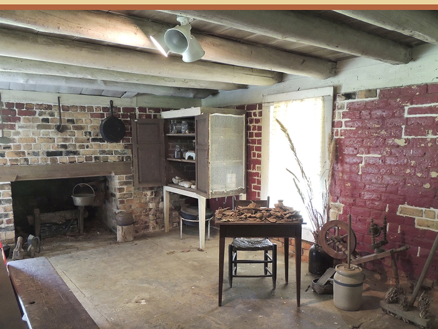 A wide brick cooking hearth on the lower floor with iron implements and a spinning wheel